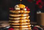 Une main versant du sirop d'érable sur une pile de pancakes