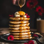 Une main versant du sirop d'érable sur une pile de pancakes