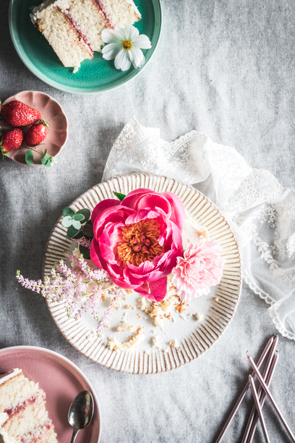 Vue de dessus d'un gâteau décoré de fleurs. juste à côté, des parts sont disposées dans de jolies assiettes roses et vertes.