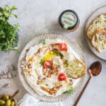 Assiette de labneh à la pulpe d'olive à la tomate vue de dessus. L'assiette est garnie de produits évoquant la Méditerrannée et une assiette de pain grillé suggère un apéro à partager.